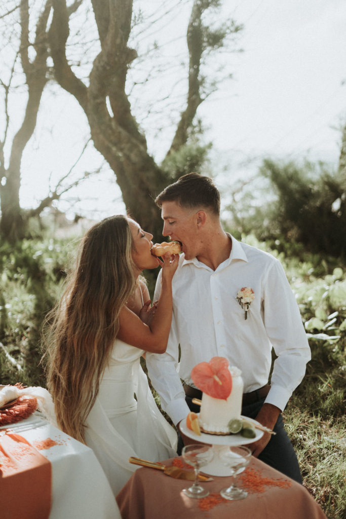 this is a young couple eloping on a beach in Hawaii. They are sharing a donut.